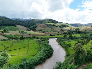 Drone view of a calm river flowing through rural farmland surrounded by hills.