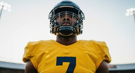 Intense portrait of a young football player wearing a helmet. Determined athlete looking at the camera with focus on a stadium field