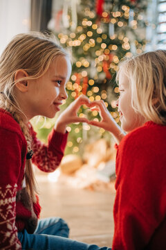 Kids in festive sweaters making heart hands by christmas tree