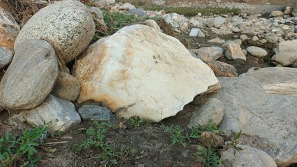 Natural rough stone textures and earthy ground with sparse green plants create a rugged outdoor...