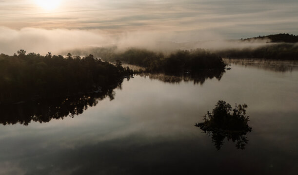 Morning mist rises over a peaceful and still lake in Maine