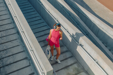 Woman in pink athletic outfit using phone while walking down outdoor stairs in a sports area