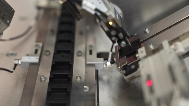 Close-up of an industrial vision system inspecting black plastic parts on a guided track using sensors and precision actuators. Includes copy space