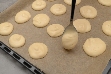 Close-up of a baking tray lined with silicone paper, spoonfuls of round biscuits being placed on it