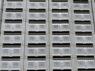 A long expanse of industrial plastic crates, neatly stacked outdoors, forms an imposing, orderly wall under a partly cloudy sky.