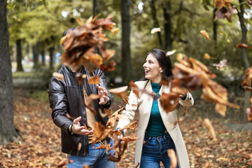 Obraz premium The couple joyfully tosses autumn leaves, celebrating the essence of love and vibrant moments shared in nature's beauty.