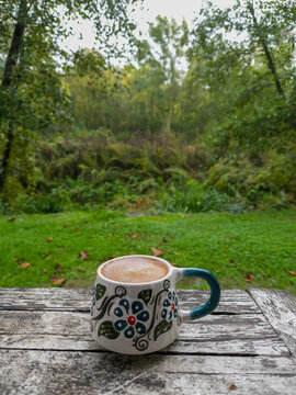 Turkish coffee in a traditional ceramic mug on a rustic wooden table with a green forest background