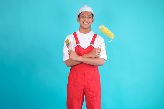 Asian Wall Painter in Overalls and Hard Hats Holding Two Kind of Paintbrush on Blue Background