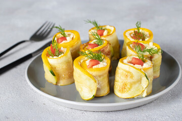 Zucchini rolls with garlic, cream cheese and tomato on gray plate