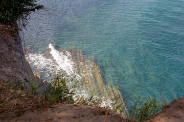 A view of a cliff on the seashore. Sea waves wash over the rocky shore.