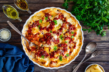 Bolognese pasta casserole - baked rigatoni noodles with bolognese sauce, mozzarella cheese and béchamel sauce on wooden table. Top view