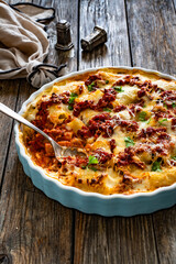 Bolognese pasta casserole - baked rigatoni noodles with bolognese sauce, mozzarella cheese and béchamel sauce on wooden table