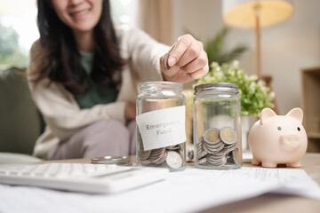 A woman putting coins into a jar labeled emergency fund with a piggy bank beside it, representing financial safety, savings planning, and personal finance management for future security.