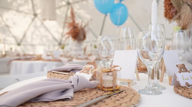 Elegant baby shower table setting with teddy bear-themed name cards, woven placemats, wine glasses, and pastel decor, creating a cozy and stylish celebration atmosphere. Baby birthday decor.
