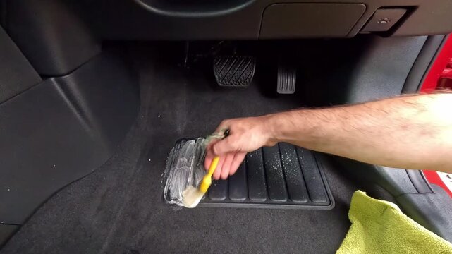 Cleaning footwell carpet plastic inside car with detailing brush and all purpose cleaner