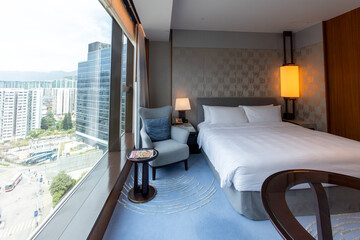 Modern hotel room interior with city view, large windows, comfortable bed, armchair, cozy ambiance,...