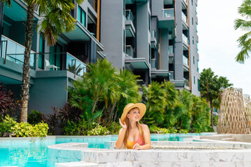 Woman in sunhat relaxing in luxury resort pool surrounded by tropical greenery and modern architecture, enjoying summer vacation. © TravelMedia