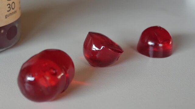 Macro close-up of red vitamin gummies on a white table showing texture and transparency under natural light.