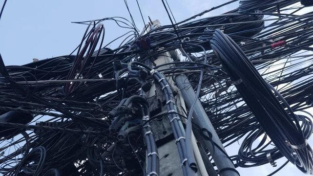 Dangerous overloaded utility pole with excessive tangled electrical wiring and communication lines creating safety hazard