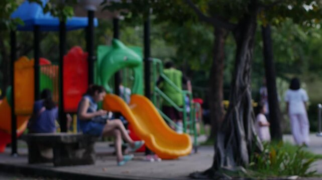 Blurred out of focus colorful children playground with slides and climbing equipment in public park surrounded by trees