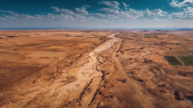 Arid landscape with sandy textures and a dry riverbed under a blue sky with clouds