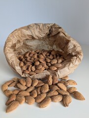 A canvas paper bag pouring raw almonds onto a white table. A top-down view of nuts and packaging.
