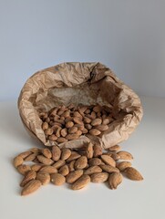 Organic almonds spilling from a rustic paper bag onto a clean white surface. A natural, wholesome food concept.