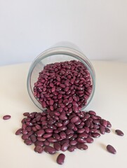 A minimalist flat-lay of red beans poured from a clear glass jar onto a pure white surface. Simple and clean.