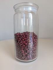 A half-full glass jar of red kidney beans, standing on a pristine white background. A simple, minimalist still life of a pantry staple.