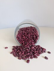 Red kidney beans pouring from a tilted glass jar onto a white surface. Simple, natural food ingredient.