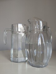 Two different shaped glass water jugs side by side on a white table. A simple, effective stock image.