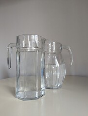Two glass water jugs with different elegant shapes, standing together on a white surface. A stylish composition.