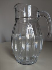 A full glass water pitcher on a white table. Practical and clean image for kitchen or restaurant themes.