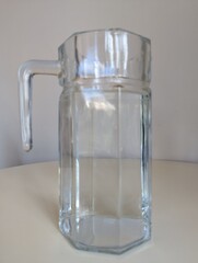 A concept image of purity and transparency. A clear glass water pitcher standing alone on a white surface.
