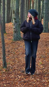 Medium shot of a woman with a dark jacket and beanie walking on a mossy hill through a pine forest during a golden hour sunset, with warm natural light filtering through the tall trees