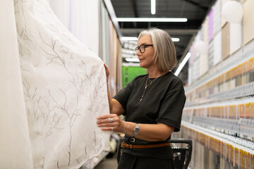 Woman selecting fabric in a modern home decor store during daylight with shelves of supplies in the background