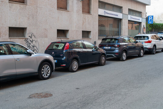 Cars lined up along a city street and parked parallel in front of a Vittoria Assicurazioni office