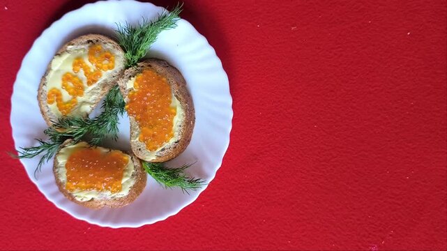 sandwich with butter and red caviar. The numbers 2026. A white plate on a red background. Dill sprigs. 2026 made of caviar on a sandwich. A woman's hand moves the plate.