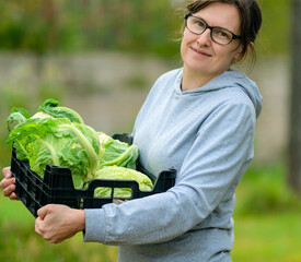 Smiling woman farmer holding a box full of fresh cauliflower during harvest season on her farm. Healthy vegetables grown naturally, organic produce rich in fiber and nutrients. © Sk Elena