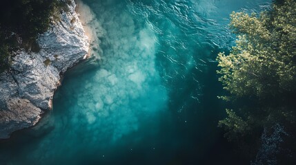 Obraz premium An aerial view of a turquoise river flowing through a rocky landscape, with a lush green tree on the right side of the frame.