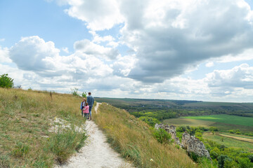 Father and daughter stand on top of hill and enjoy beautiful scenery of green hills under blue...