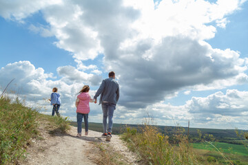 Father and daughter on top of hill and enjoy beautiful scenery of green hills under blue cloudy sky.