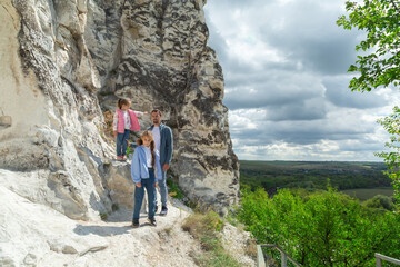Father and daughters stand on top of mountain and enjoy beautiful scenery of green hills under blue...