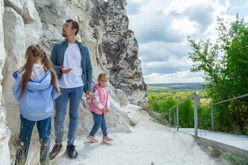 Father and daughters stand on top of mountain and enjoy beautiful scenery of green hills under blue...