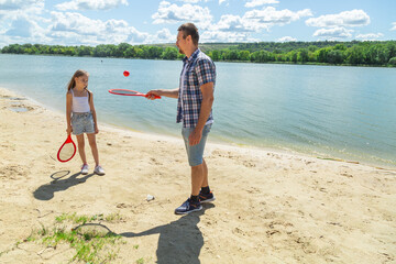 Father teaching beach tennis to daughter while standing on sand on beach
