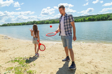 Father teaching beach tennis to daughter while standing on sand on beach