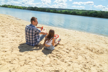 Father and daughter sitting on sand on beach after playing tennis