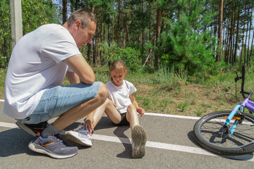 Father helping her little daughter after falling off bicycle in forest