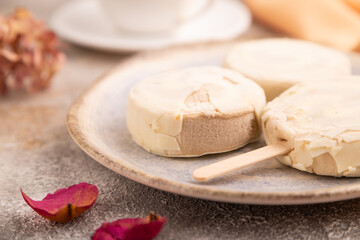 Сhocolate Ice cream in white glaze, cup of coffee, on brown concrete and orange textile, side view, close up, selective focus