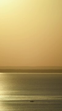 Fishing boat moving on the surface of a large lake, clear sky and calm water, horizon, warm evening light.